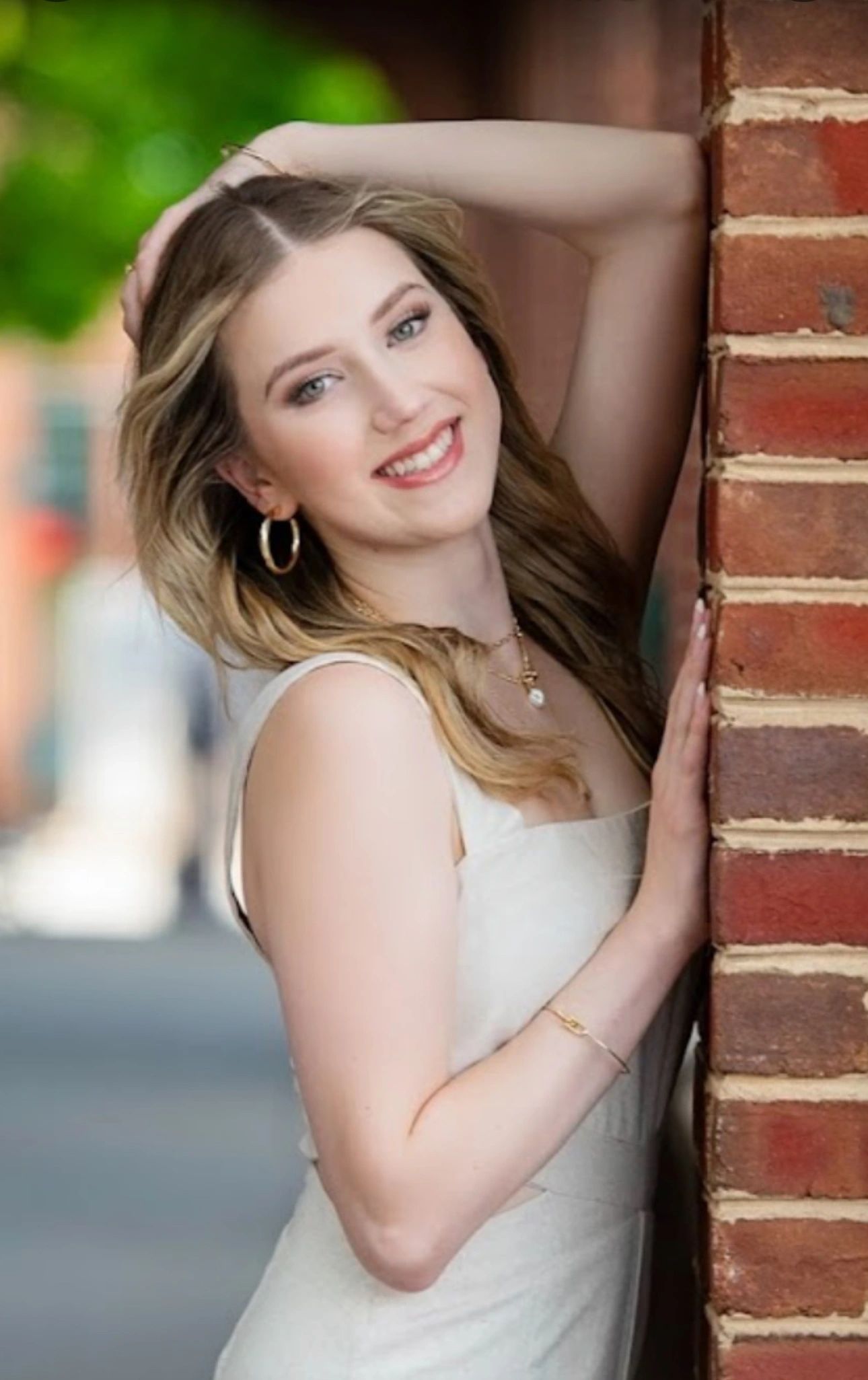A senior portrait against a brick wall, soft waves and a natural makeup finish