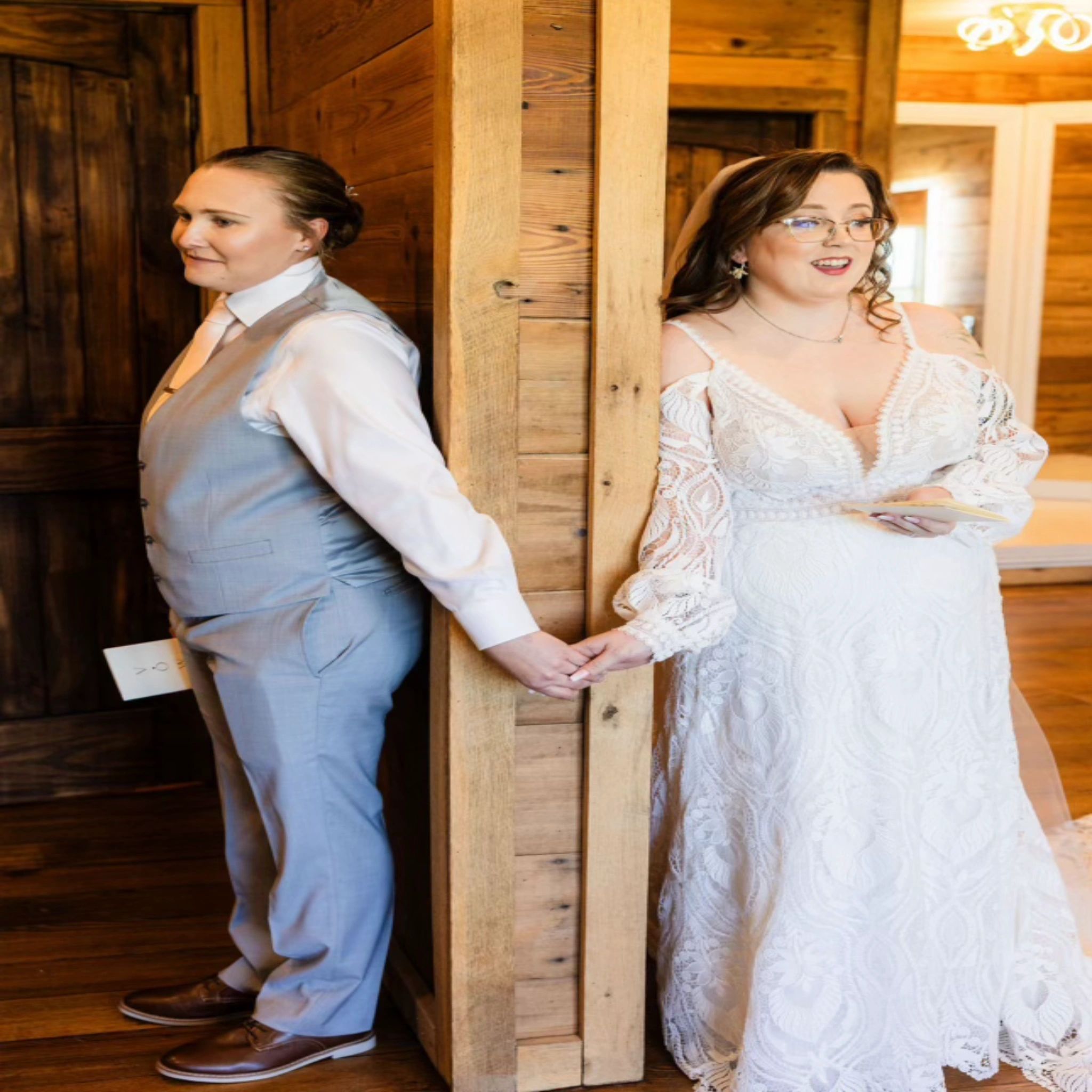 A couple standing back to back around a timber post, holding hands for their first look